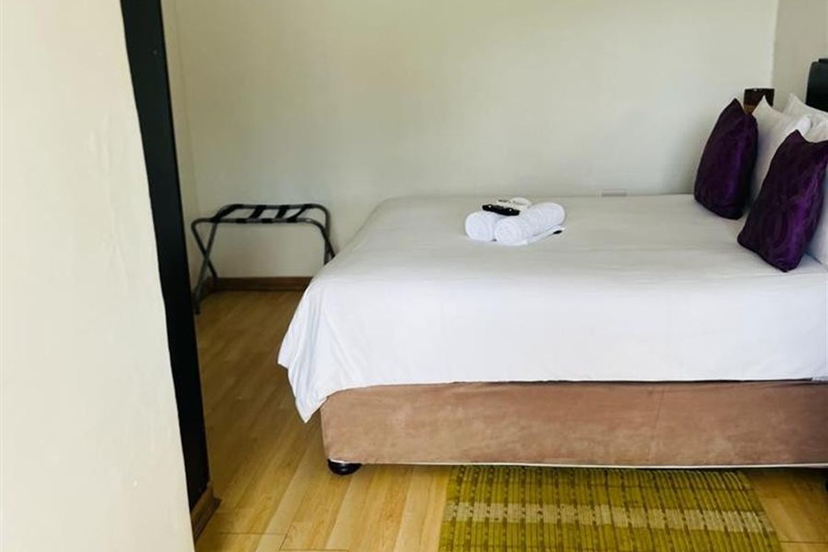 A bedroom featuring light-toned laminate flooring, crown molding, and a wall-mounted air conditioning unit.