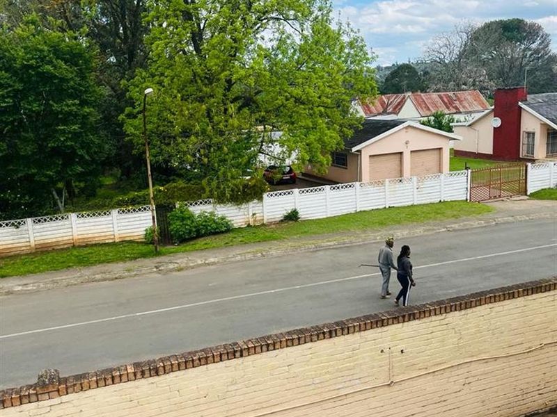An elevated street view showing the property's boundary wall, paved driveway, and the surrounding neighbourhood street scene.