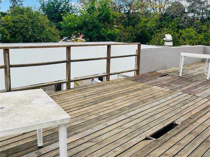 An elevated outdoor wooden deck featuring a balustrade and parapet wall, currently showing signs of wear and requiring maintenance to the decking surface.