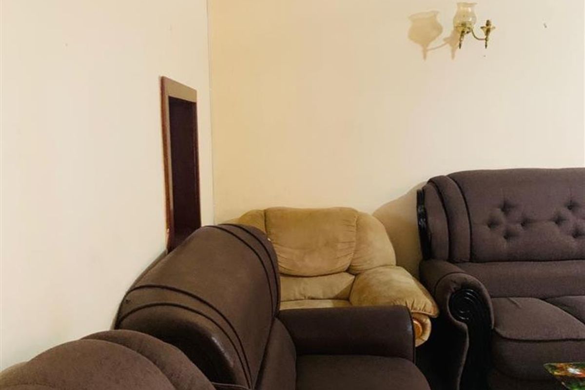 A living room area featuring tiled flooring, decorative coving, and a wall-mounted light fixture, showing signs of water damage on the wall.