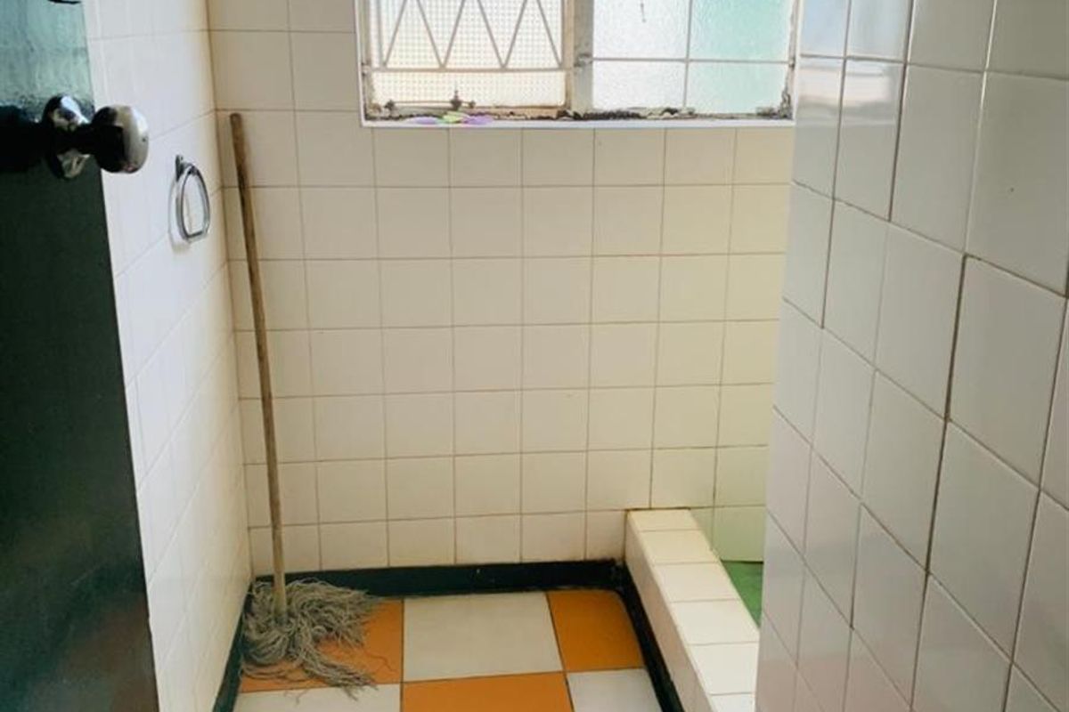 A dated bathroom featuring tiled walls and flooring with a built-in shower base and security-grilled window, requiring modernization and cosmetic updates.