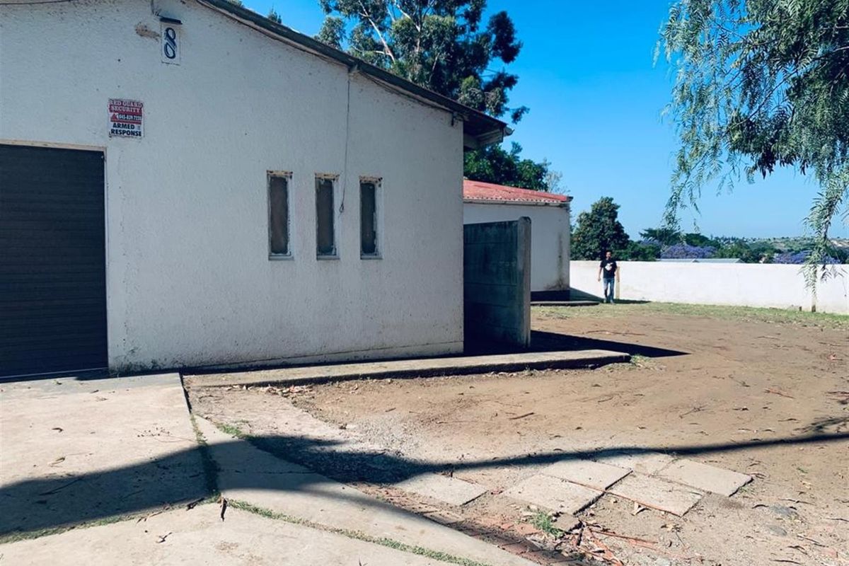 Rear exterior view of the property featuring a concrete driveway, perimeter wall, and garage access with visible wear to the exterior finishes.