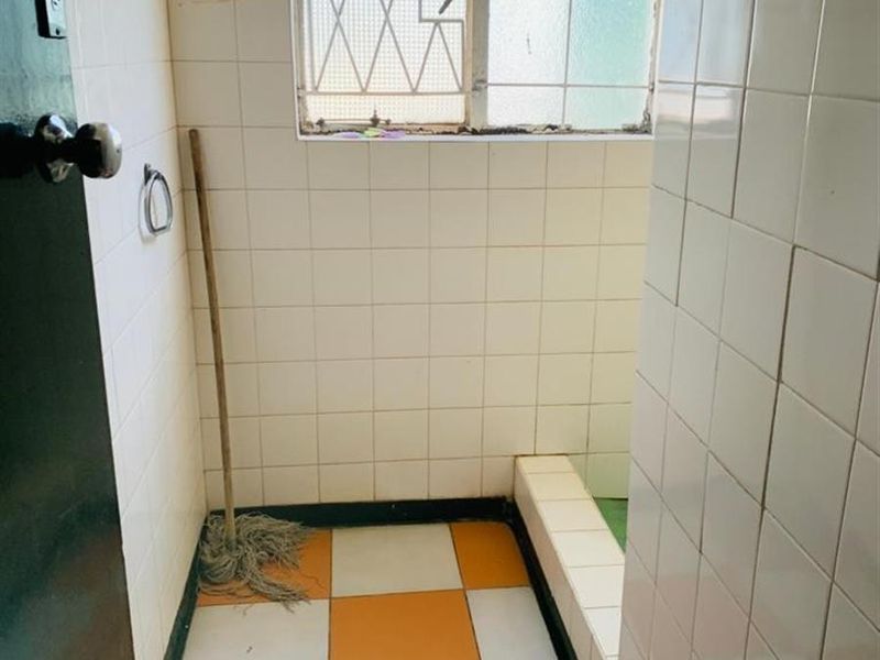 A dated bathroom featuring tiled walls and flooring with a built-in shower base and security-grilled window, requiring modernization and cosmetic updates.