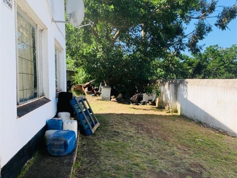 A view of the rear exterior area featuring a boundary wall, concrete pathway, and mounted satellite dishes against the side of the house.