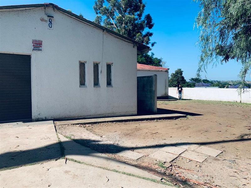 Rear exterior view of the property featuring a concrete driveway, perimeter wall, and garage access with visible wear to the exterior finishes.