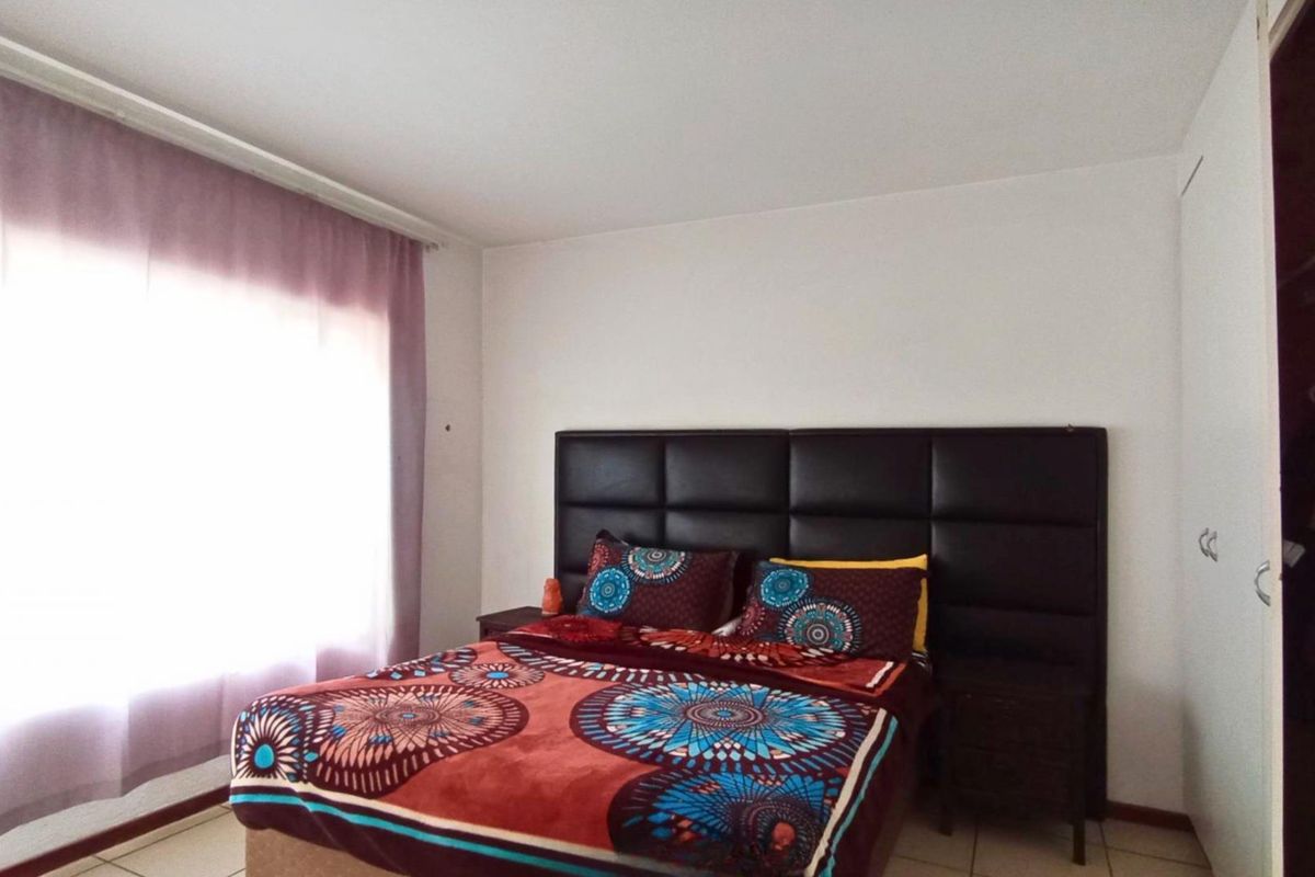 A bedroom featuring tiled flooring, built-in cupboards, and a large window allowing natural light.