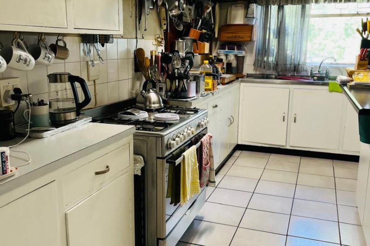 Functional kitchen featuring tiled flooring, built-in cabinetry, a gas stove with extractor fan, and a double basin sink with window view.