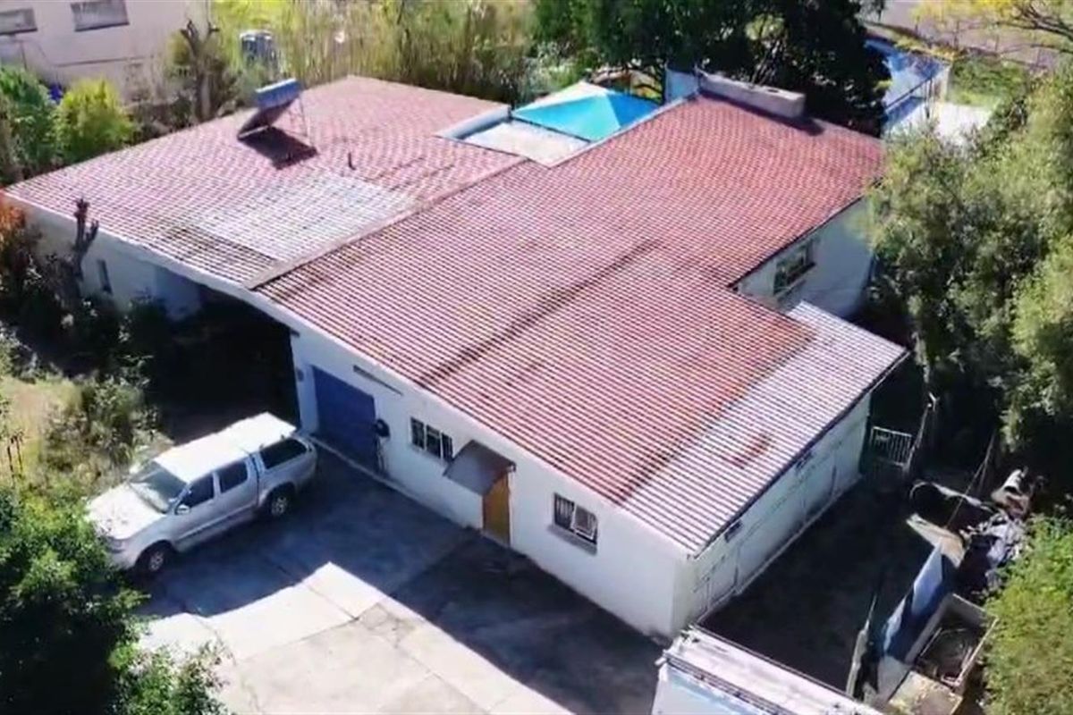 Aerial view of a residential property featuring a corrugated metal roof, solar water heating system, and a concrete driveway.