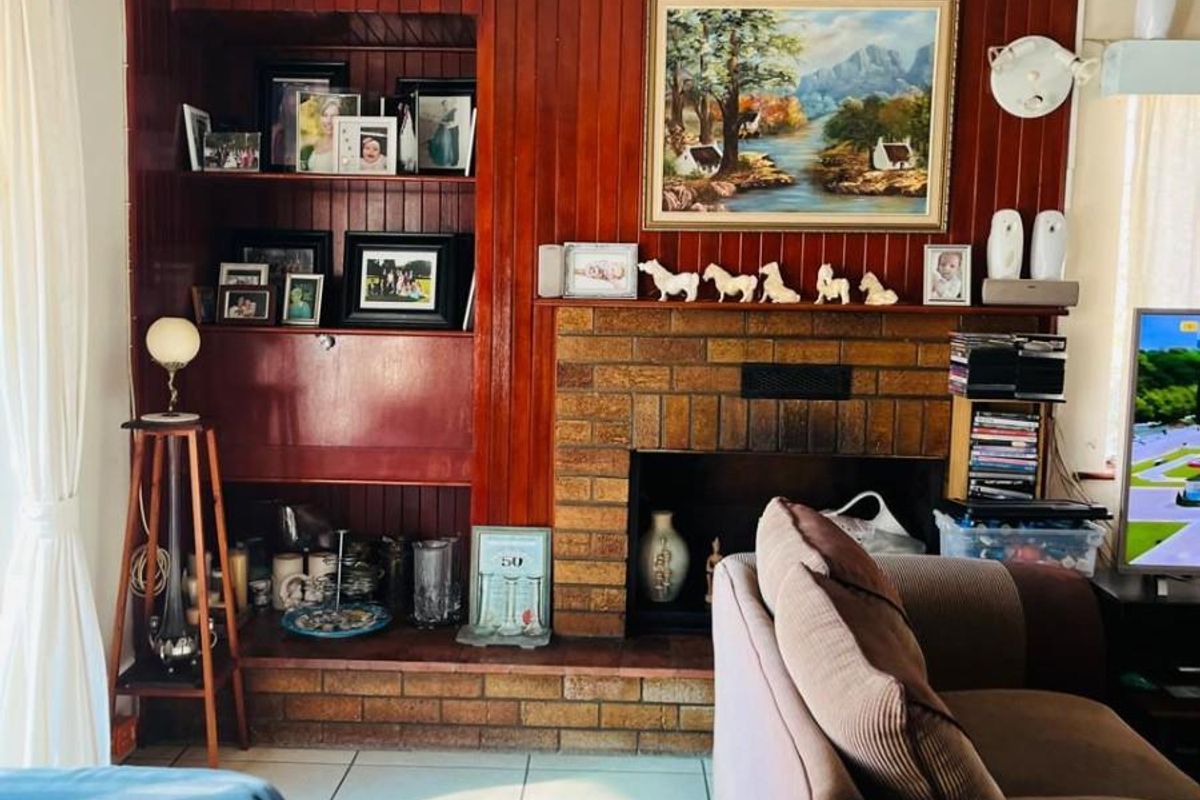 Living room featuring a traditional brick fireplace, timber wall paneling, and built-in shelving, finished with tiled flooring.