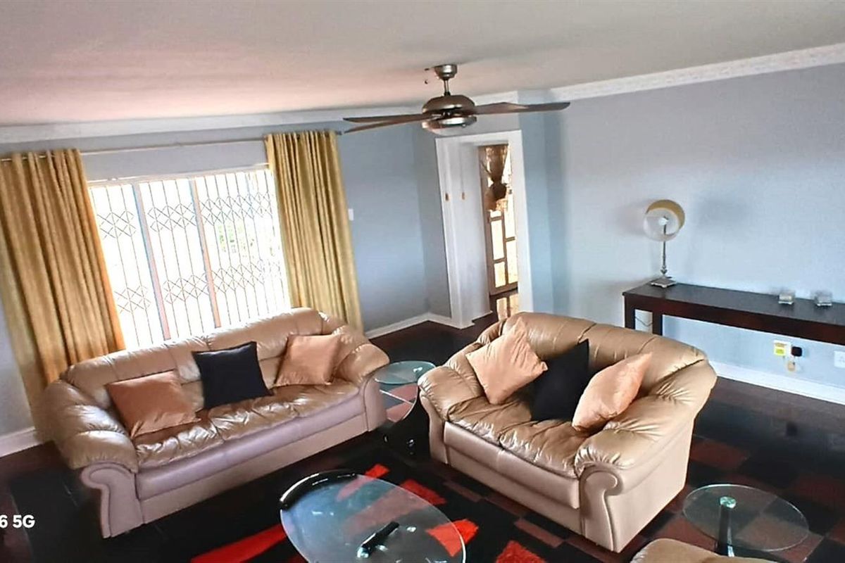 Spacious living room featuring dark hardwood flooring, crown molding, and a ceiling fan, with large windows protected by security gates.