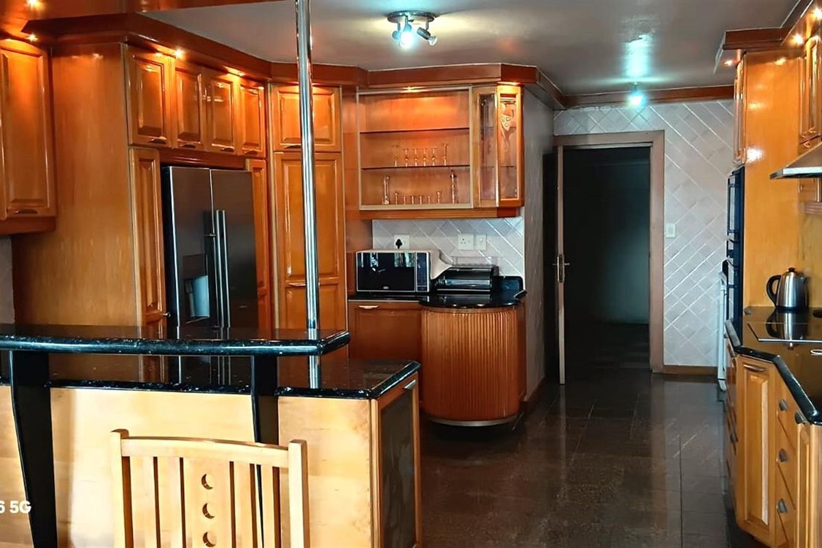 A traditional kitchen featuring warm-toned wooden cabinetry, dark granite countertops, and tiled flooring, offering a functional layout with integrated storage and prep space.