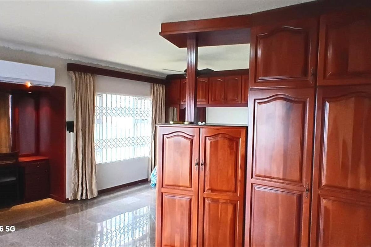 A bedroom featuring extensive built-in wooden cabinetry, a dedicated study nook, tiled flooring, and a wall-mounted air conditioning unit.