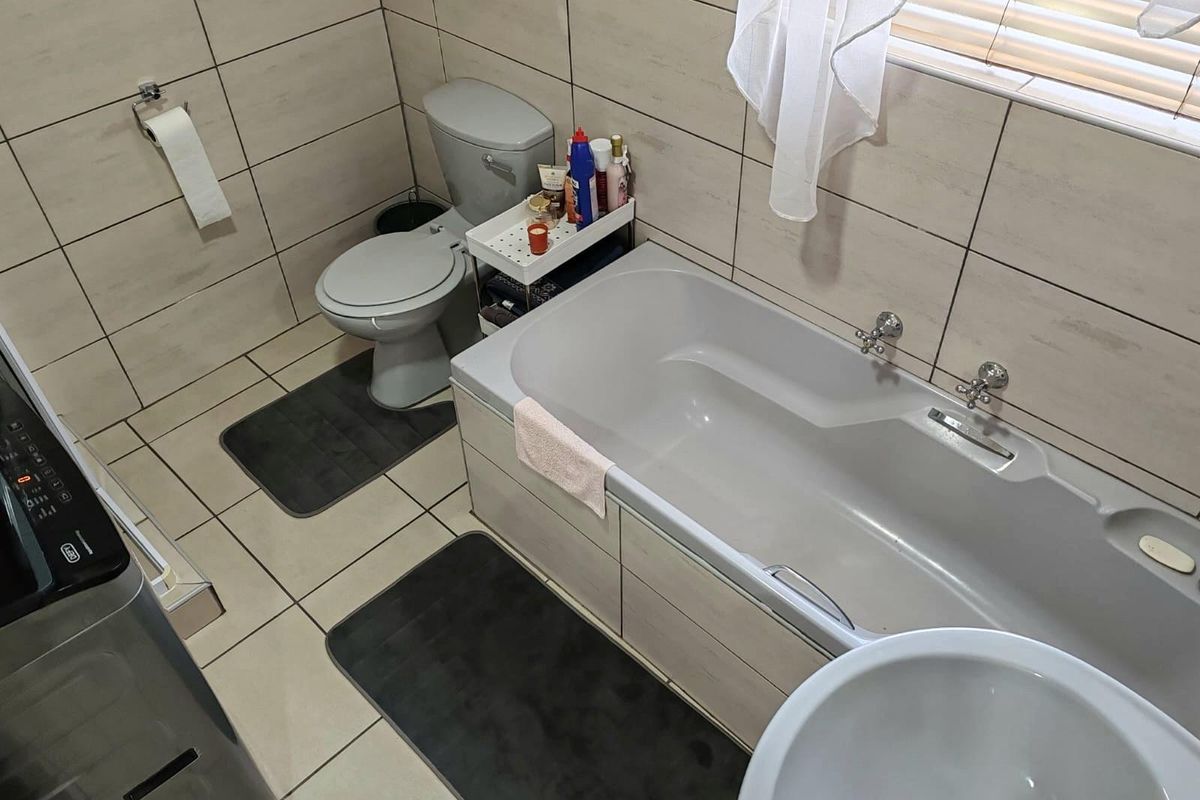 A functional bathroom featuring floor-to-ceiling wall tiles, a standard bathtub with chrome taps, a toilet, and a basin.