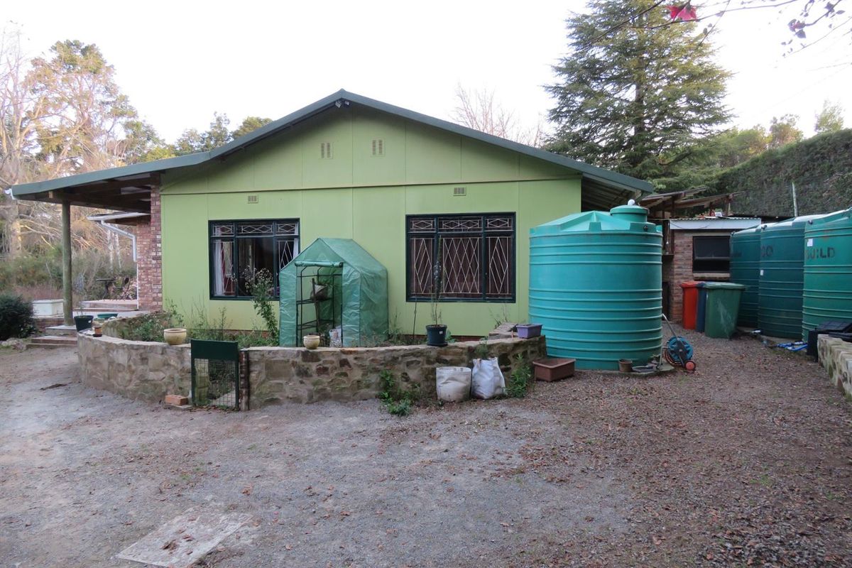 Rear view of the property featuring a green exterior facade, stone retaining wall, and multiple large water storage tanks in the garden area.