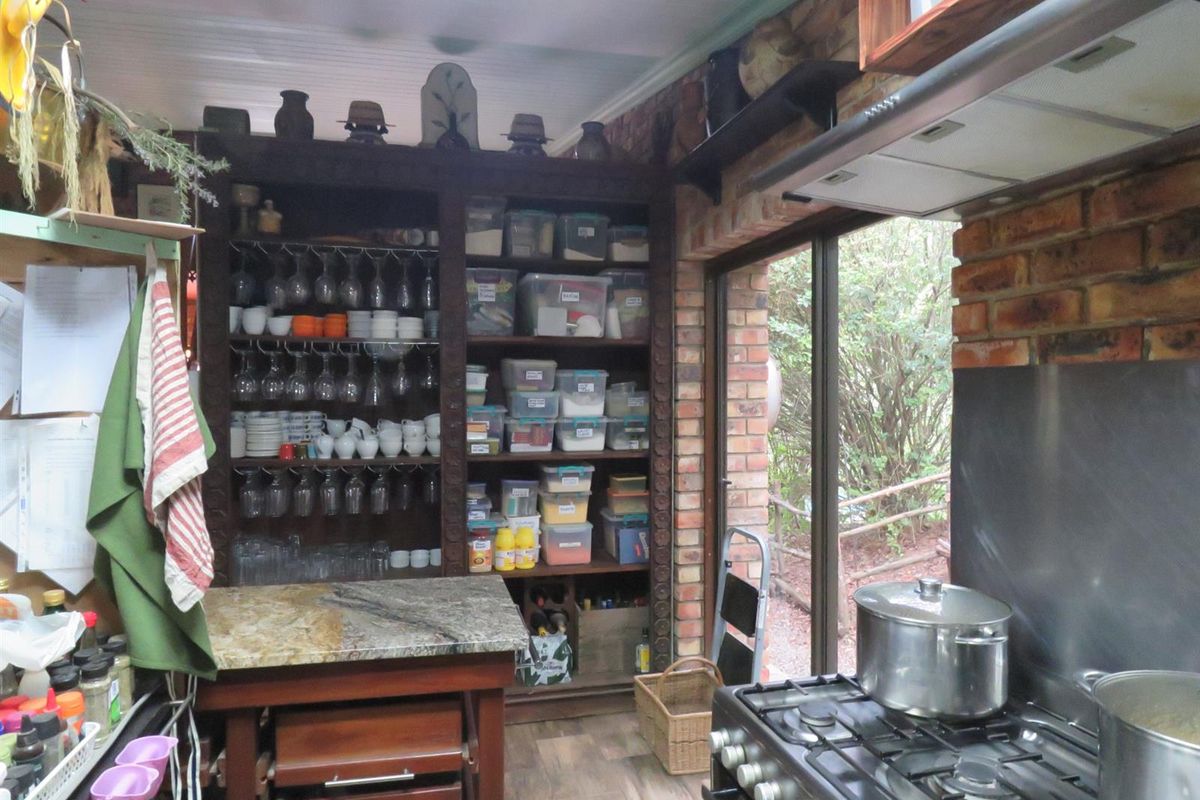A rustic kitchen featuring exposed brick walls, built-in wooden shelving, a gas stove with extractor fan, and a stone-topped prep island.