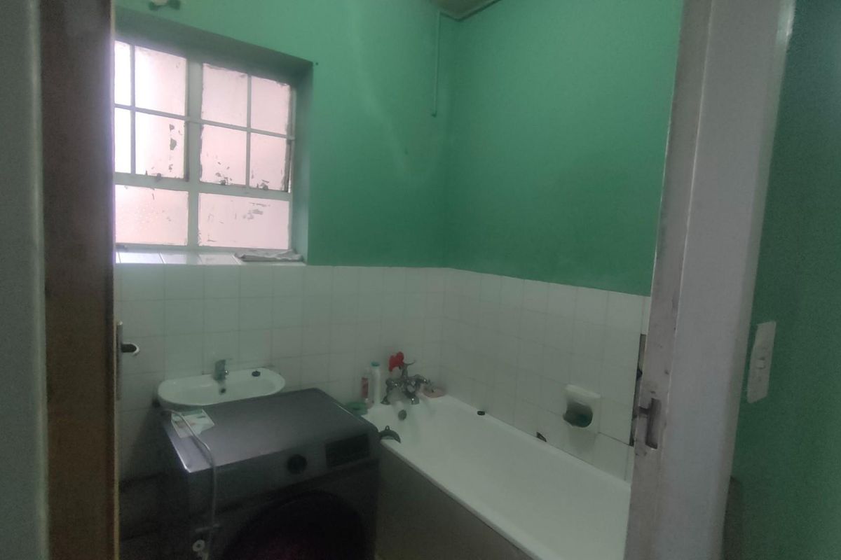 A functional bathroom featuring a standard bathtub, wall-mounted basin, and window, requiring cosmetic updates to modernize the space.