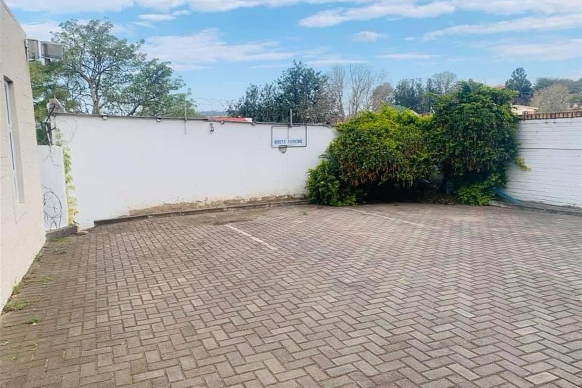 A paved guest parking area enclosed by a boundary wall with established greenery.