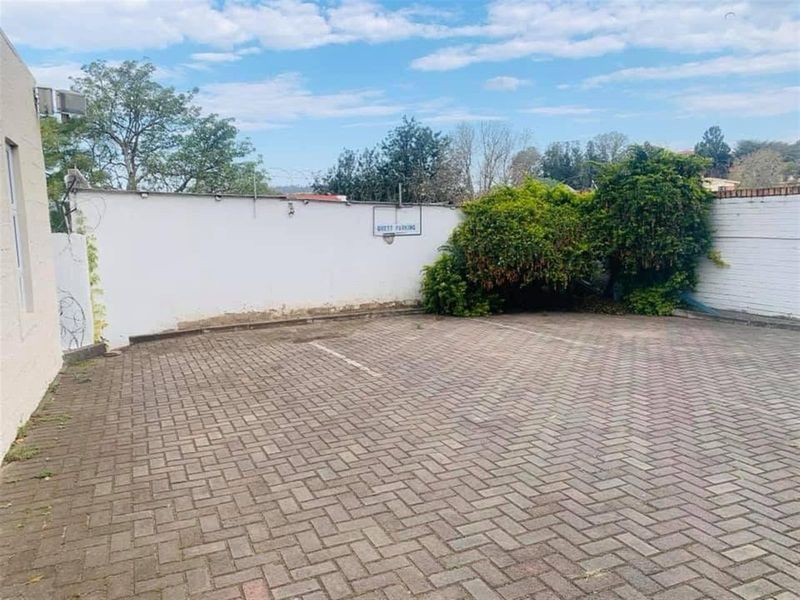 A paved guest parking area enclosed by a boundary wall with established greenery.