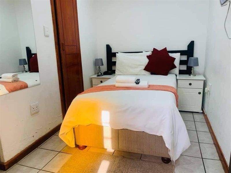 A compact bedroom featuring tiled flooring, a built-in wooden door, and a wall-mounted mirror, providing a functional space for guests.