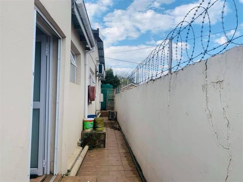 A narrow exterior side passage featuring a tiled walkway, perimeter wall with razor wire, and exterior building access.
