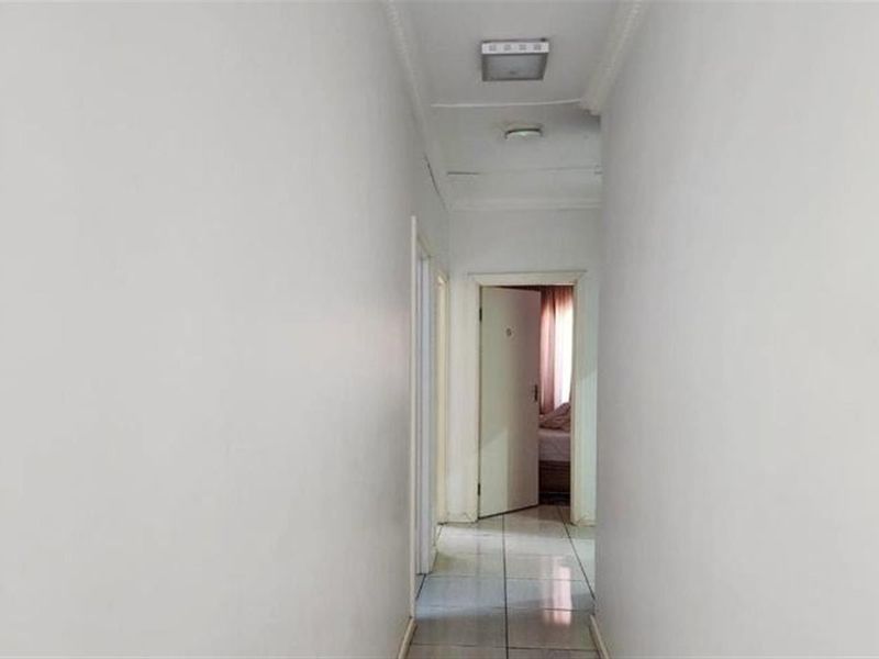 A narrow interior hallway featuring tiled flooring and a ceiling-mounted light fixture, showing signs of wear on the ceiling surface.