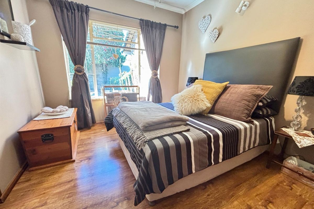 A cozy bedroom featuring warm-toned laminate flooring, neutral wall finishes, and a large window allowing for natural light.