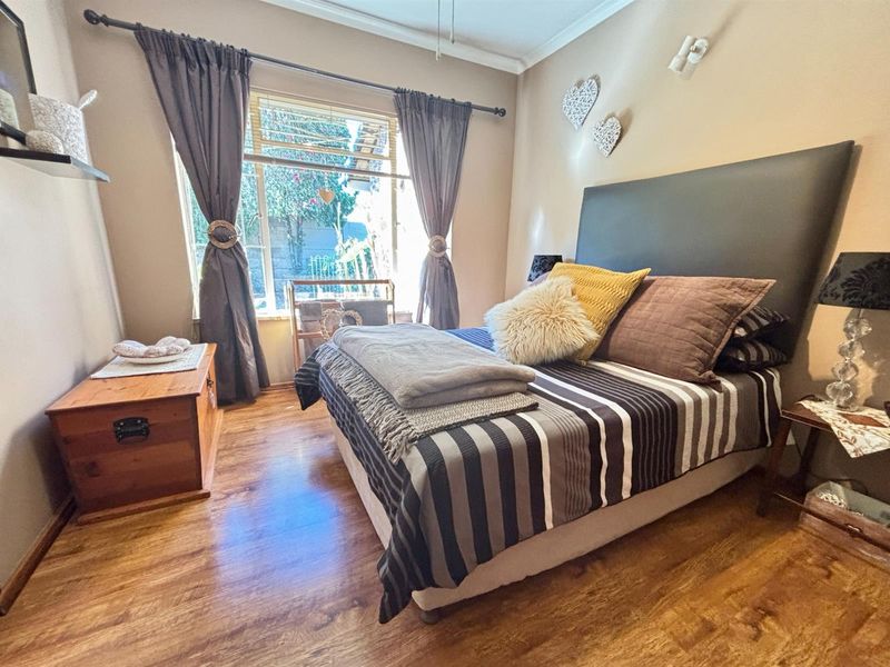 A cozy bedroom featuring warm-toned laminate flooring, neutral wall finishes, and a large window allowing for natural light.