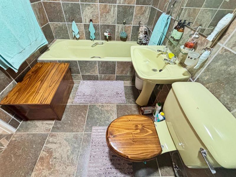 A compact bathroom featuring a vintage-style green bathtub, matching pedestal basin, and toilet, complemented by full-height stone-look wall tiling and floor tiles.