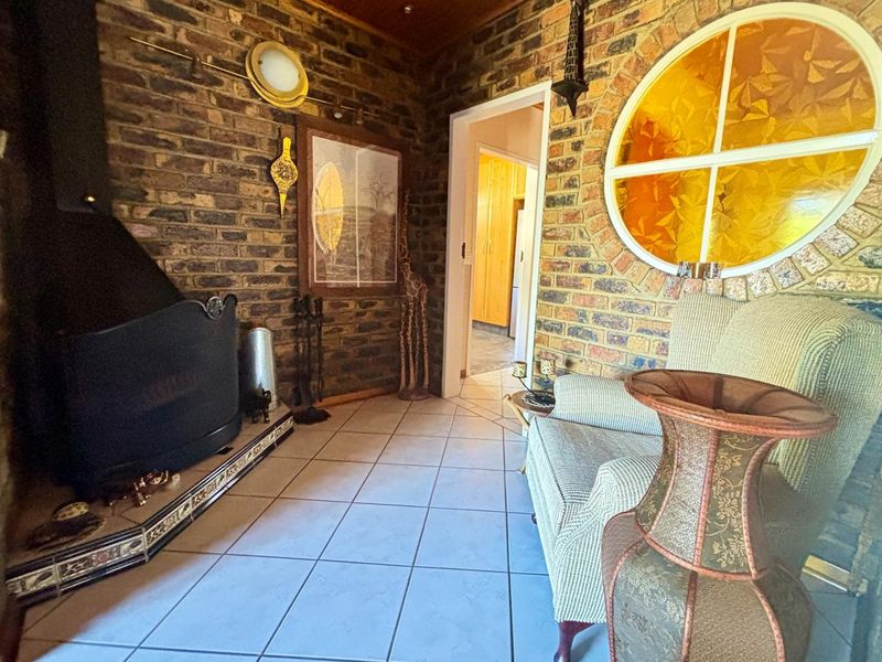 A cozy living room featuring exposed brick walls, a wood-burning fireplace, tiled flooring, and a distinctive circular feature window.