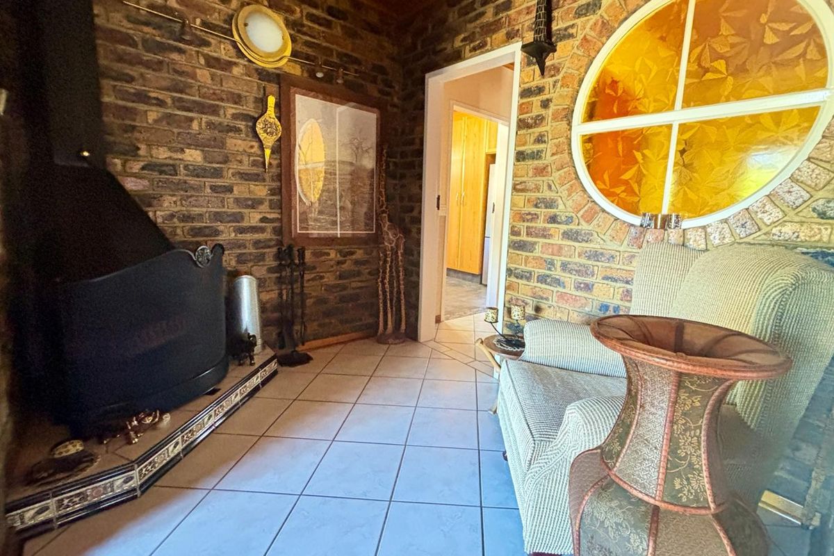 A cozy living room featuring exposed brick walls, a wood-burning fireplace, tiled flooring, and a distinctive circular feature window.