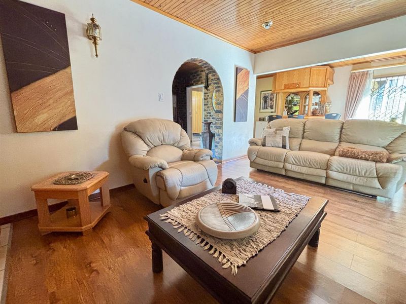 A living room featuring a timber-clad ceiling, laminate flooring, and a distinctive brick archway leading to an adjacent space with a built-in bar.
