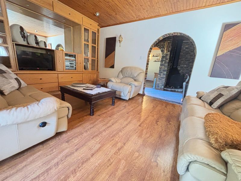 Living room featuring wood-paneled ceilings, laminate flooring, built-in cabinetry, and a distinctive brick archway leading to a fireplace area.