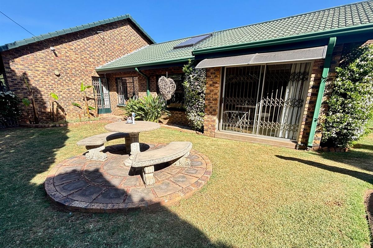 Rear garden area featuring a brick facade, tiled roof, solar water heater, and a paved patio space with direct access via sliding glass doors.