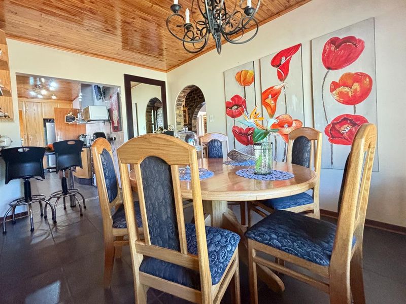 Dining area featuring a warm timber ceiling, wrought iron chandelier, and an arched brick doorway leading to the kitchen.