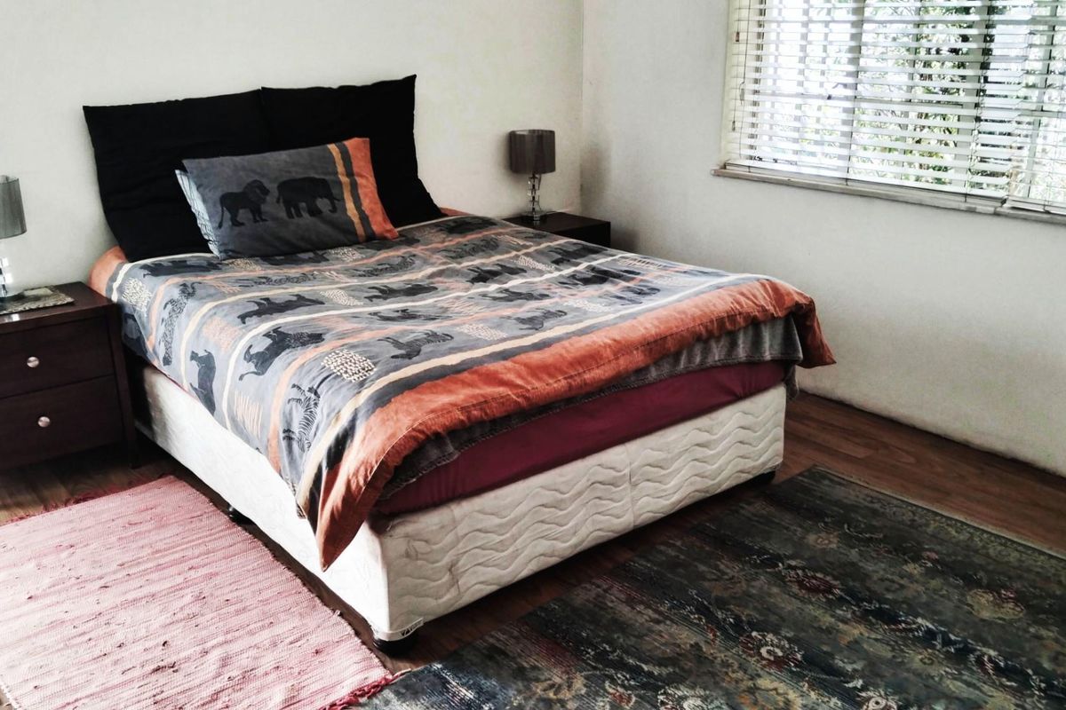 A bedroom featuring wood-look flooring and horizontal window blinds, providing a functional and neutral space for rest.