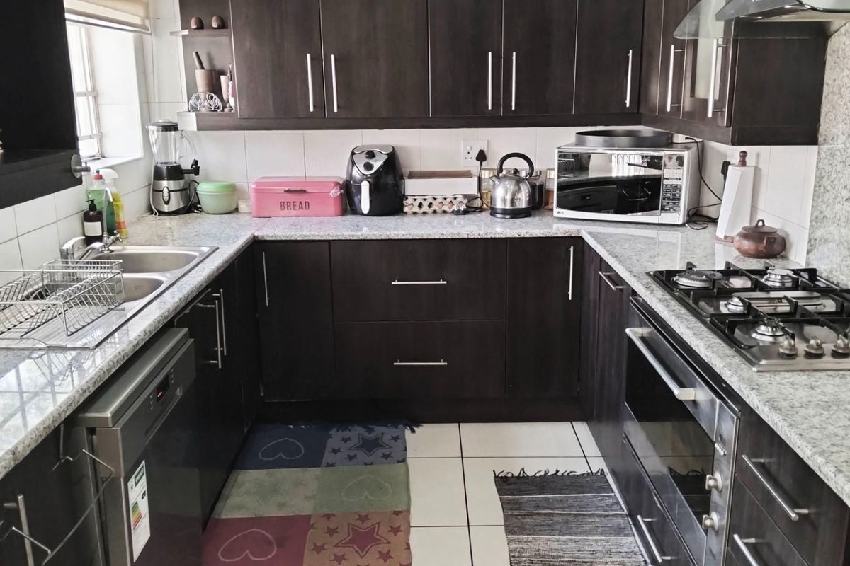 A functional U-shaped kitchen featuring dark cabinetry, granite countertops, a built-in oven, gas hob, and stainless steel sink.