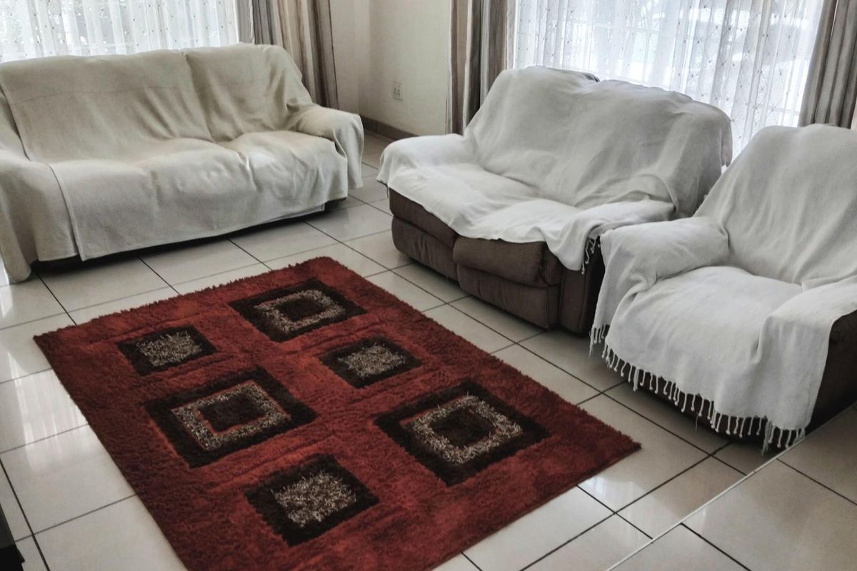 A spacious living room featuring neutral ceramic floor tiles and large windows with sheer curtains, providing a bright and functional living space.