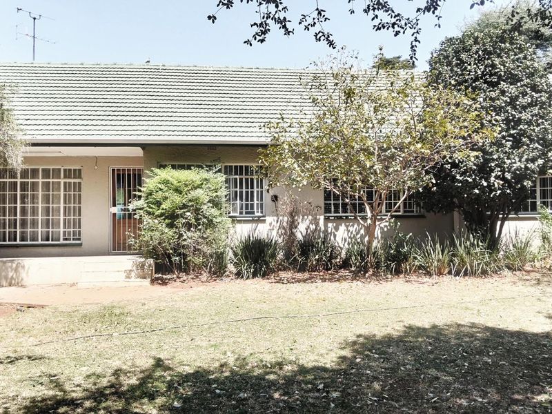 A view of the rear exterior of the house, featuring a tiled roof, security bars on windows, and a spacious garden area.