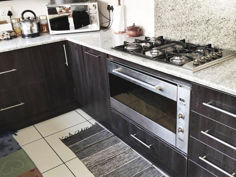 A functional kitchen featuring dark wood cabinetry, granite countertops, a built-in oven, and a gas hob with a tiled backsplash.