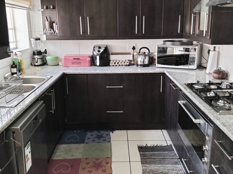 A functional U-shaped kitchen featuring dark cabinetry, granite countertops, a built-in oven, gas hob, and stainless steel sink.