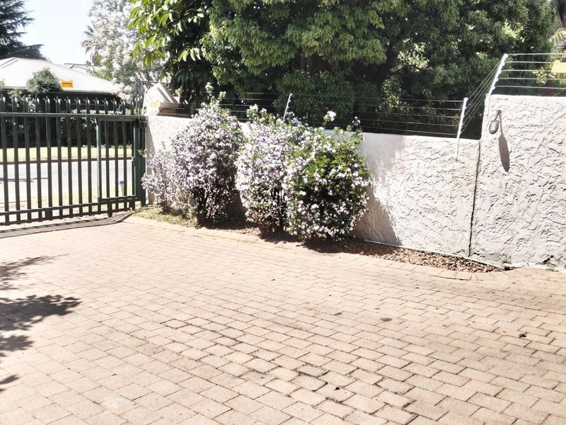 A paved driveway area featuring a secure metal gate and a perimeter boundary wall topped with electric fencing.