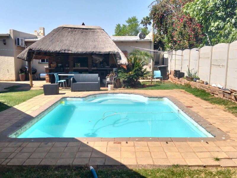 A private backyard featuring a swimming pool and a thatched lapa entertainment area with built-in brick braai facilities.