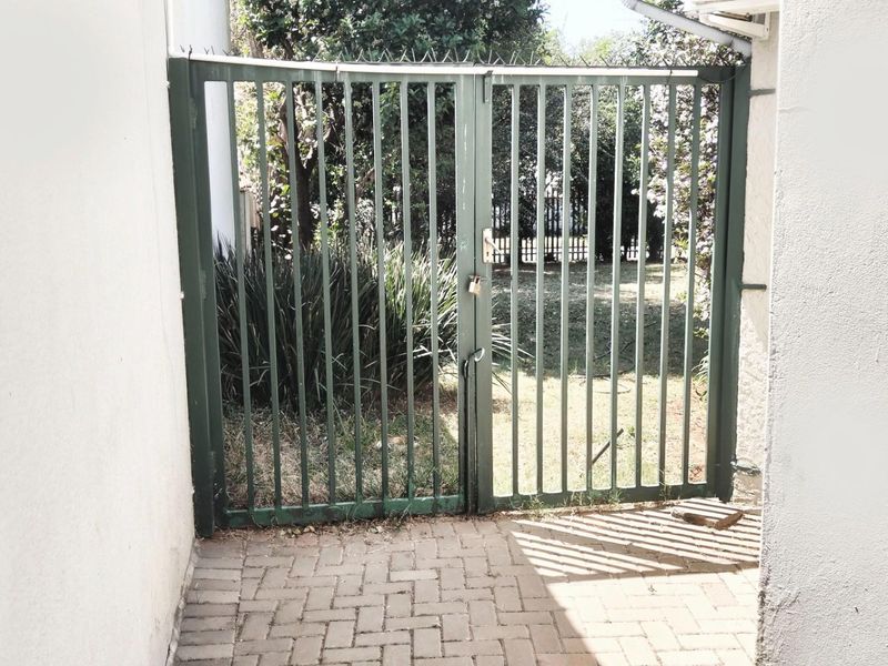 A secure metal gate providing access to the rear garden area, featuring paved flooring and perimeter walling.