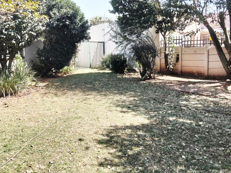 A private rear garden area featuring established trees, perimeter boundary walls, and a metal security gate.