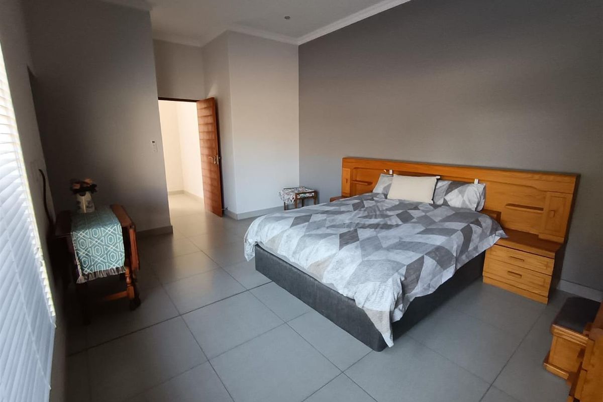 A spacious bedroom featuring neutral grey walls, large format floor tiles, and a built-in wooden headboard with integrated bedside tables.