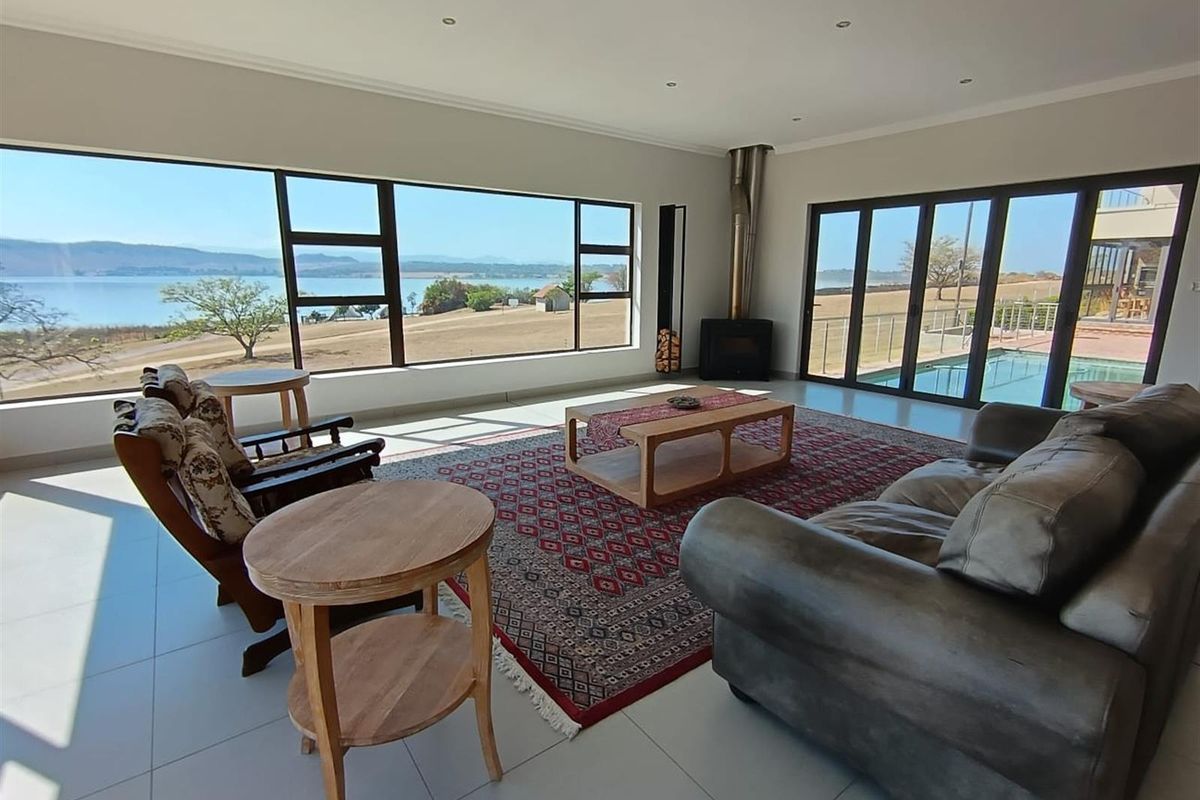 Spacious living area featuring large floor-to-ceiling windows with panoramic lake views, a modern freestanding fireplace, and direct access to the outdoor pool deck.