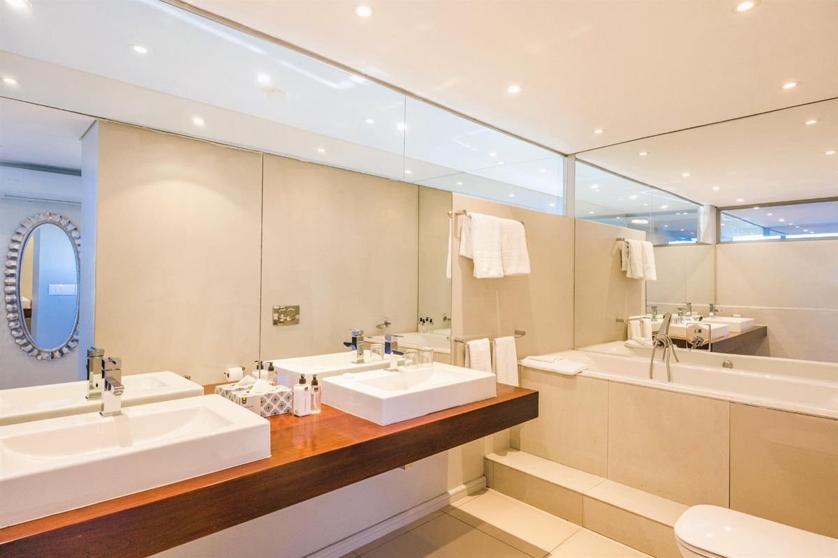 Modern bathroom featuring a double vanity with vessel sinks, a built-in bathtub, and extensive wall-to-wall mirror paneling.