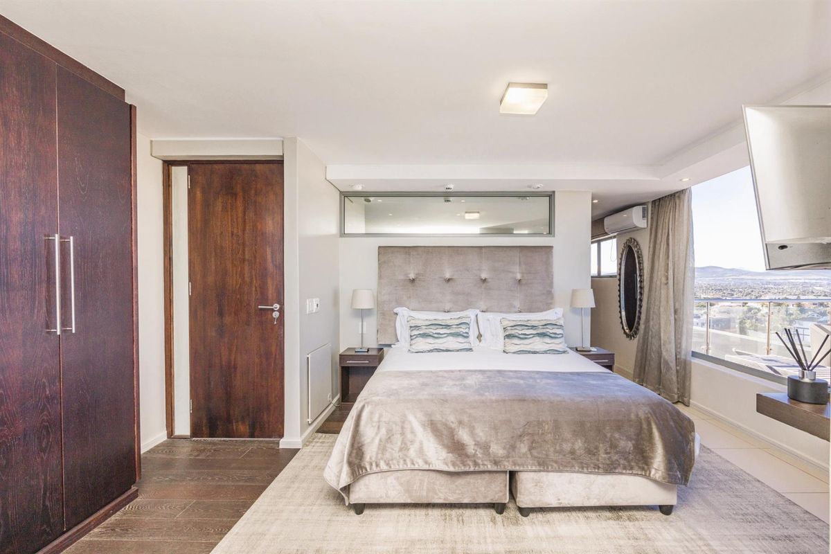 A well-maintained bedroom featuring built-in dark wood cabinetry, a large window with expansive views, and a wall-mounted air conditioning unit.