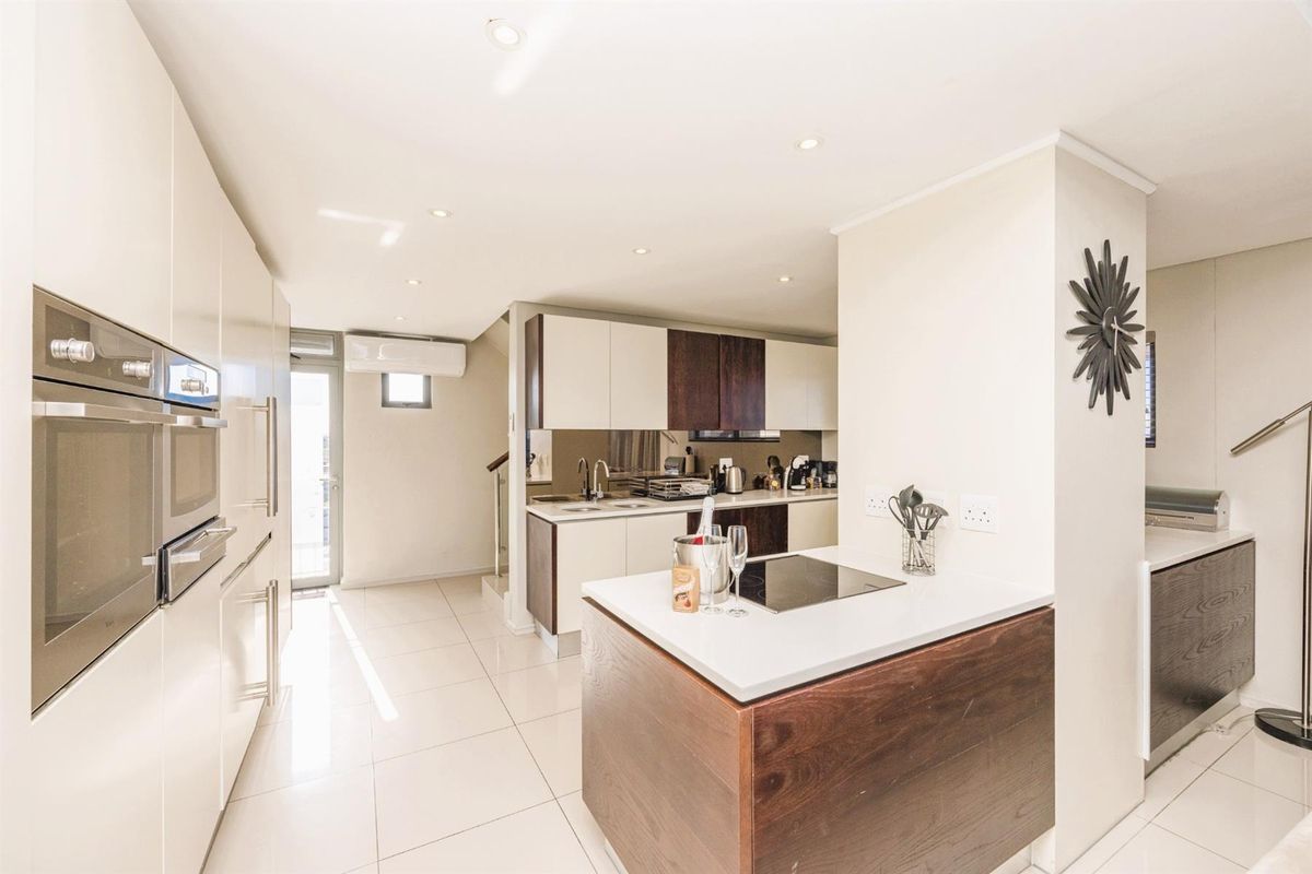 Modern kitchen featuring two-tone cabinetry, integrated oven, induction hob on a central island, and sleek tiled flooring with recessed lighting.