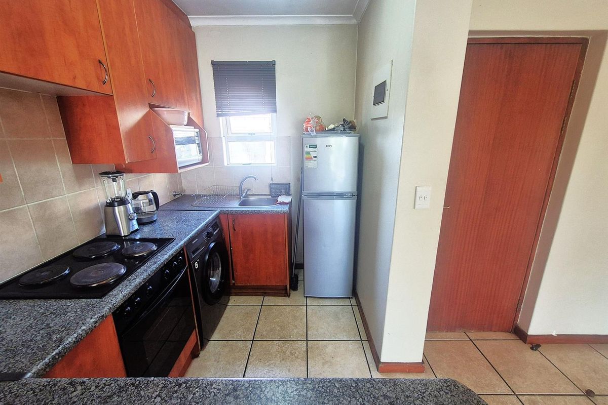 Compact kitchen featuring wood-look cabinetry, granite-style countertops, integrated electric hob and oven, and tiled flooring.